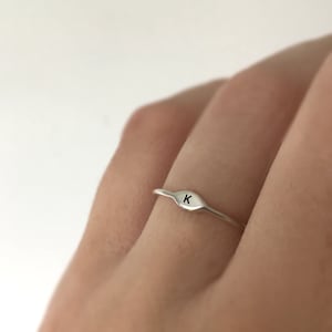 May include: A silver ring with a small, oval-shaped band featuring the letter "K" engraved on the top.