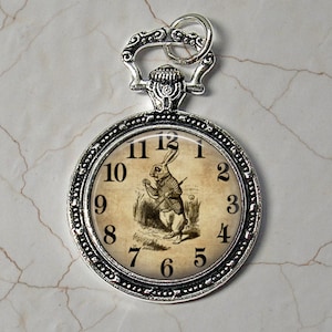 May include: Silver pocket watch pendant with a white rabbit illustration and Roman numeral clock face. The rabbit is holding a pocket watch and has a waistcoat on.