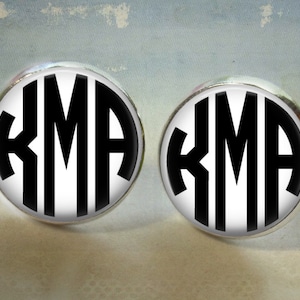 May include: A pair of silver cufflinks with black and white round monograms. The monogram is the letters "KMA" in a classic font.
