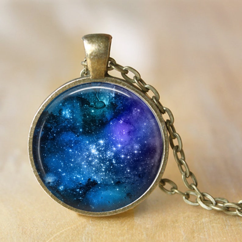 May include: A silver chain necklace with a round pendant featuring a galaxy print with blue, purple, and white colors.