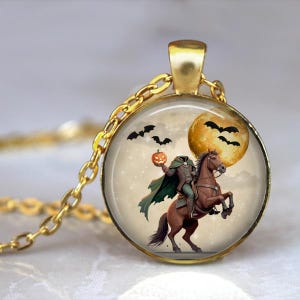 Puede incluir: Collar con colgante dorado con un dije redondo que muestra una ilustración de Halloween. El dije representa una figura sin cabeza a caballo, sosteniendo una calabaza, con murciélagos y una luna llena. La cadena es dorada.