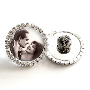 May include: A silver pin with a clear glass cabochon featuring a vintage black and white photograph of a couple. The cabochon is surrounded by a circle of clear rhinestones.