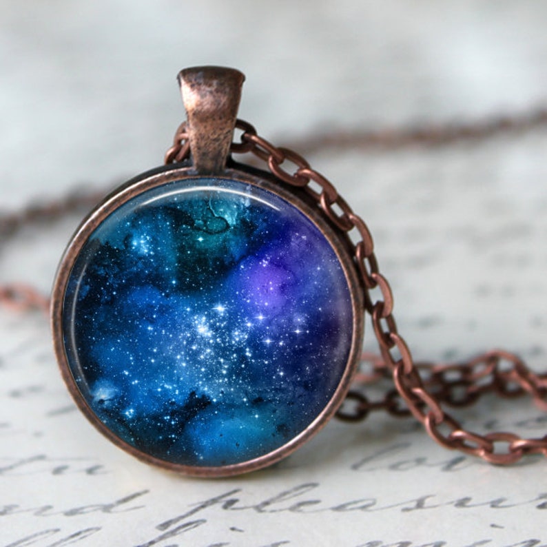 May include: A copper necklace with a round pendant featuring a galaxy image. The pendant has a dark blue background with white stars and purple and green nebulae.