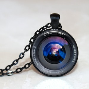 Op de afbeelding: Een zwarte camera lens hanger ketting met een blauwe en paarse afbeelding in de lens. De lens is gemarkeerd met "20mm 1:3.8 AUTO VIVITAR WIDE-ANGLE No.22007482".