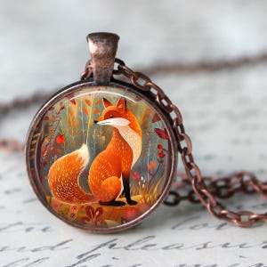 May include: A copper chain necklace with a round glass pendant featuring a hand-painted illustration of a fox sitting in a forest setting. The fox is orange with a white chest and a bushy tail. The background is a mix of green, brown, and orange colors.