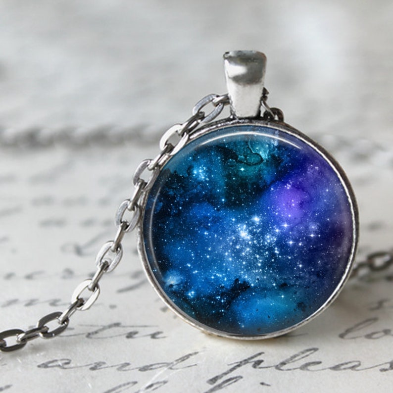 May include: A silver chain necklace with a round glass pendant featuring a blue and purple galaxy with white stars.