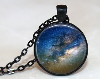 May include: A black chain necklace with a round glass pendant featuring a photograph of the Milky Way galaxy. The galaxy is a swirling mass of blue, white, and gold stars against a dark blue background.