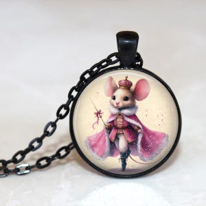 May include: Black pendant necklace featuring a round charm with a whimsical illustration of a mouse in a pink cape and crown. The mouse holds a wand. The chain and pendant frame are black.
