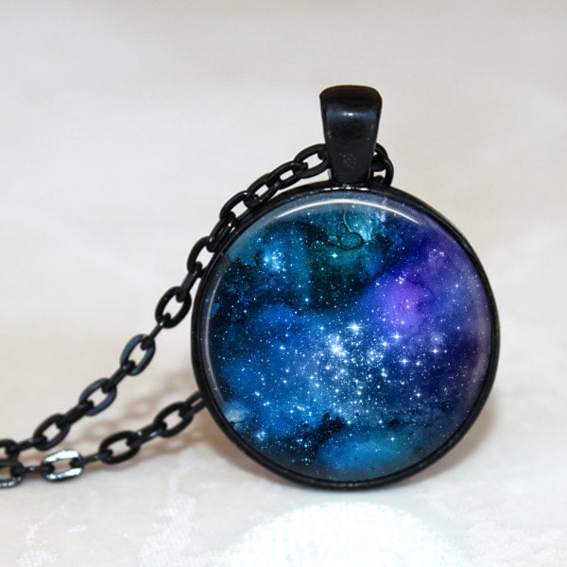 May include: A black chain necklace with a round glass pendant featuring a blue and purple galaxy with white stars.