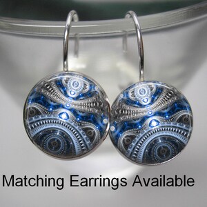 May include: A pair of round, silver-toned earrings with a blue, black, and white abstract design. The earrings have a hook closure. The text "Matching Earrings Available" is displayed below the earrings.