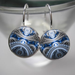 May include: A pair of silver earrings with blue and white geometric patterns. The earrings are round and have a silver hook.