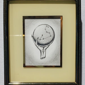 May include: A framed black and white pencil drawing of a hand holding a sphere with a constellation of stars inside.