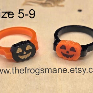 May include: Two Halloween-themed rings. One ring is orange with a black pumpkin face, and the other is black with an orange pumpkin face. The rings are size 5-9. The website address www.thefrogsmane.etsy.com is visible.