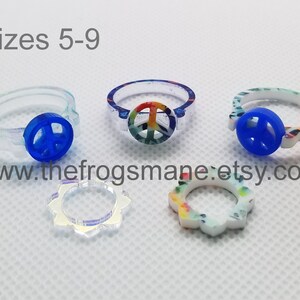 May include: A set of five peace sign rings in various colors and designs. The rings are made of plastic and are available in sizes 5-9. The rings feature a peace sign symbol in the center. The rings are perfect for adding a touch of peace and love to any outfit.