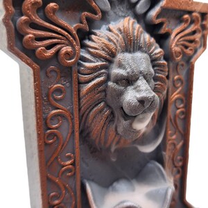 May include: A gray and copper colored incense burner with a lion's head design. The lion's head is carved in detail and has a small opening for incense to be placed. The incense burner is decorated with ornate copper colored designs.