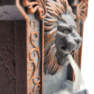 May include: A gray and brown ceramic incense burner shaped like a lion's head with intricate details. Smoke flows from the lion's mouth.