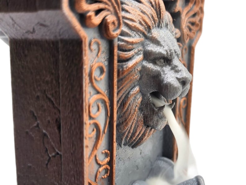 May include: A gray and brown ceramic incense burner shaped like a lion's head with intricate details. Smoke flows from the lion's mouth.