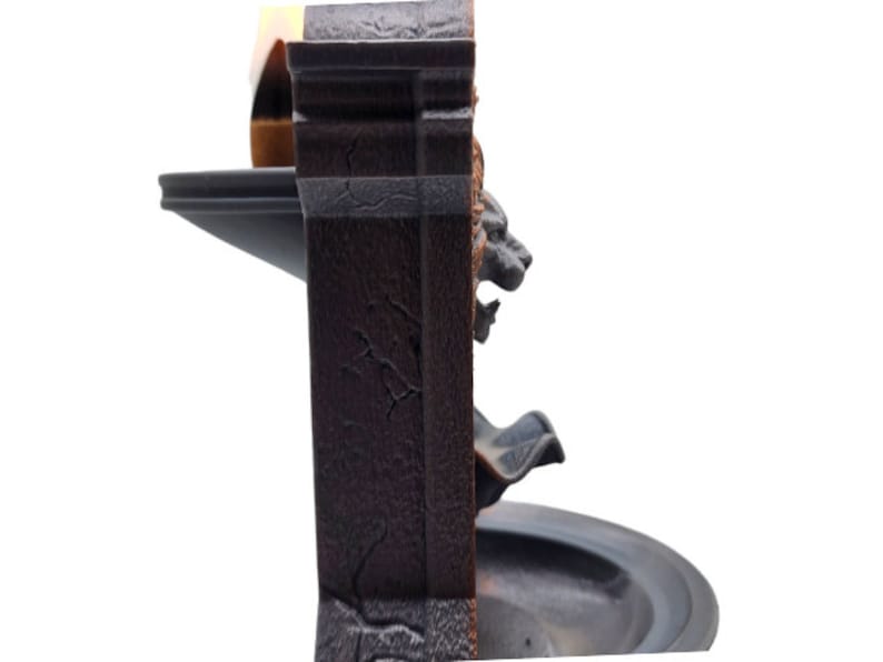 May include: A black and brown tabletop fountain with a lion head design. The fountain has a tiered design with a small basin at the top and a larger basin at the bottom. The fountain is made of a textured material that resembles stone.
