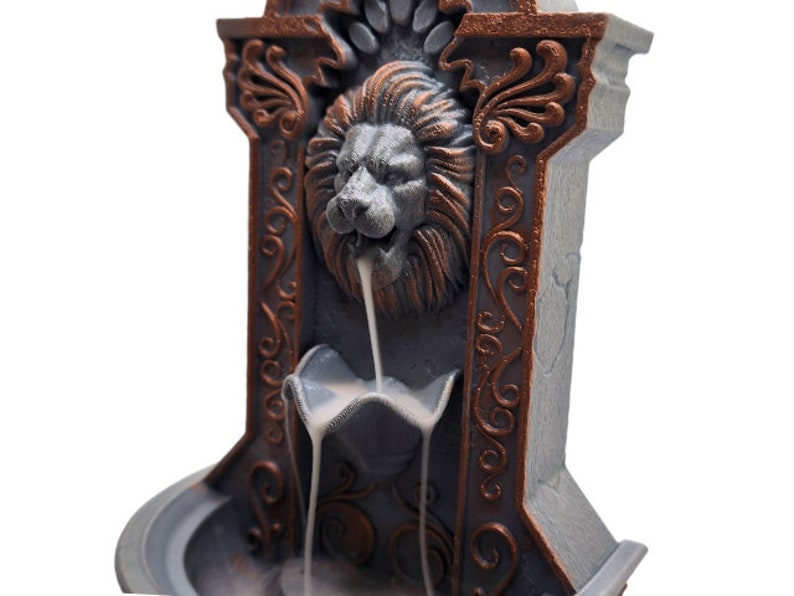 May include: A gray and copper-colored incense burner shaped like a lion's head with ornate details. The incense flows down from the lion's mouth into a basin below.
