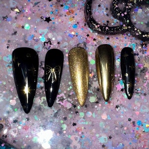May include: A black and gold glitter Hello Kitty-shaped nail polish holder with six nail tips in black and gold.