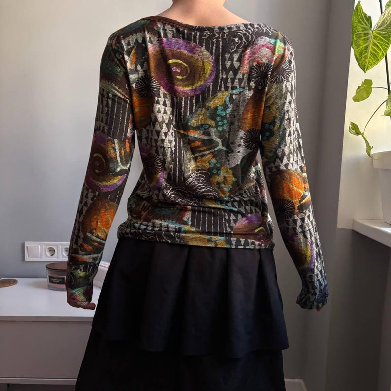 Puede incluir: Top de manga larga con un estampado abstracto colorido con detalles en naranja, morado y turquesa. Se combina con una falda negra escalonada. El dise&ntilde;o incluye formas geom&eacute;tricas y motivos florales.