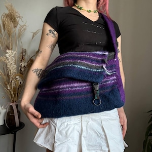 Peut inclure: Sac à bandoulière fait à la main avec fermeture à rabat. Le sac présente une palette de couleurs de rayures horizontales bleu foncé, violet et gris. La bandoulière est violette unie. Le sac a une boucle métallique et un porte-clés.