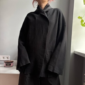 May include: A black, open-front jacket with a shawl collar. The jacket has long sleeves and a relaxed fit. The fabric appears to be a textured, woven material. The jacket is part of a two-piece outfit.