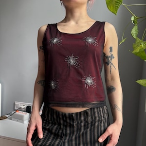 May include: A white ceramic mug with a black handle and the text "But First, Coffee" in a bold, black font. The mug is set against a blurred background, suggesting a cosy setting.