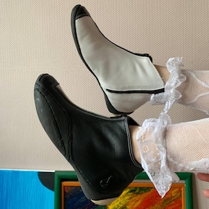 May include: A pair of ankle boots, one black and one white, with a zipper on the side. The boots are made of leather and have a pointed toe.