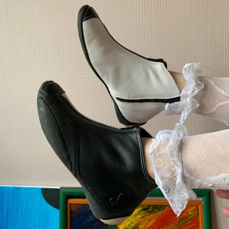 Puede incluir: Un par de botines, uno negro y uno blanco, con una cremallera en el lateral. Los botines son de cuero y tienen una punta puntiaguda.