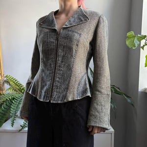 Op de afbeelding: Een jas met lange mouwen, een ritssluiting in het midden, een brede kraag en een peplumzoom. Het kledingstuk is geconstrueerd met een combinatie van een grijs acid-wash denim middenpaneel en zijpanelen met een gestructureerd visgraatpatroon.