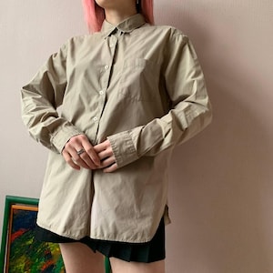 May include: A long-sleeved, light brown button-down shirt with a single pocket on the left side. The shirt is made of a soft, lightweight fabric and has a relaxed fit.