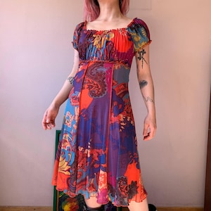 Peut inclure: Une robe colorée à motifs avec un col carré et des manches courtes bouffantes. La robe présente un mélange de motifs cachemire et floraux orange, bleus et violets. La robe a un corsage ajusté et une jupe fluide, parfaite pour l'été.