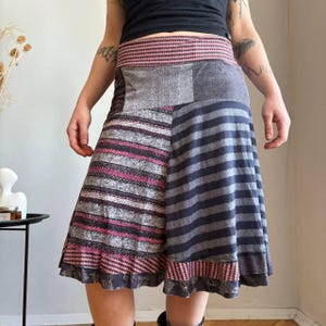 Peut inclure: Jupe patchwork avec différents motifs et couleurs. La jupe a une large ceinture rayée rose et blanche. Les panneaux de la jupe présentent des tissus à rayures et à motifs gris, roses et bleus. L'ourlet est fini avec une bordure à motifs.