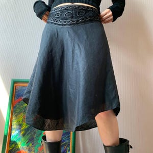 K&ouml;nnte beinhalten: Schwarzer Rock mit dekorativem, besticktem Bund. Der Rock hat eine ausgestellte Silhouette und einen leicht asymmetrischen Saum. Die Person tr&auml;gt schwarze Stiefel. Der Rock ist ca. 60 cm lang.