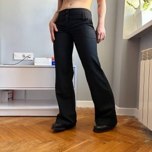 Puede incluir: Pantalones negros acampanados con cierre de dos botones. Los pantalones tienen un diseño clásico y están hechos de una tela suave. Los pantalones se combinan con zapatos negros. Una adición versátil a cualquier guardarropa.