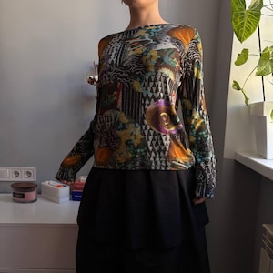 Puede incluir: Top de manga larga con un estampado abstracto colorido en tonos naranja, turquesa, morado y negro. Se combina con una falda negra. El dise&ntilde;o presenta formas geom&eacute;tricas y motivos florales.