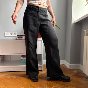 May include: A pair of black trousers featuring a high-waisted design with a structured waistband, belt loops, and a front button and zipper closure. The pants have a straight-leg cut that falls to the ankles, crafted from a textured fabric.