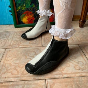 Puede incluir: Un par de botines de cuero negro y blanco con cremallera en la parte delantera. Las botas tienen una punta redonda y una suela gruesa.