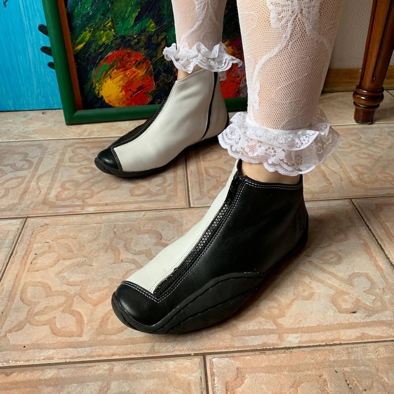 Puede incluir: Un par de botines de cuero negro y blanco con cremallera en la parte delantera. Las botas tienen una punta redonda y una suela gruesa.