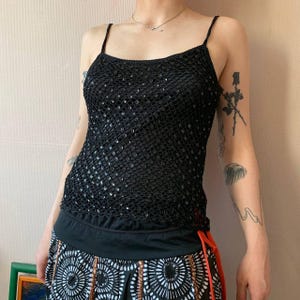 May include: Black sequined camisole top with thin spaghetti straps. The top has a mesh-like design with small, reflective sequins. The bottom portion of the top is a solid black fabric. The model is wearing a patterned skirt.