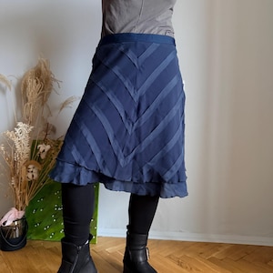 May include: A navy blue skirt with a chevron design. The skirt has a layered, ruffled hem and a fitted waist. The skirt is paired with black leggings and boots. The skirt is made of a lightweight fabric.