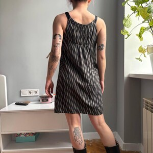 May include: A black and white patterned dress with spaghetti straps. The dress has a vertical diamond pattern and a gathered bodice. The dress is knee-length and appears to be made of a lightweight fabric.