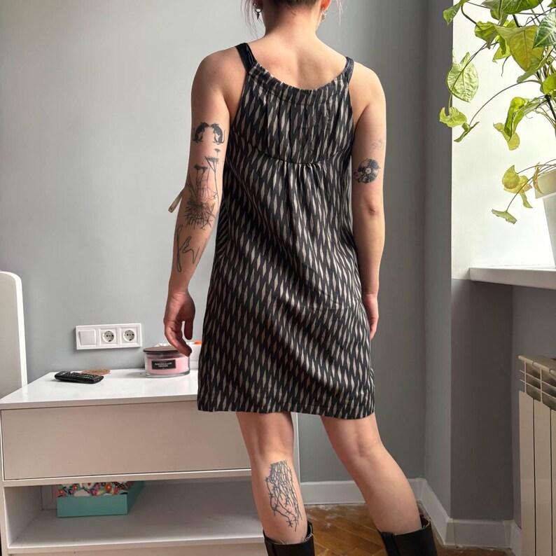 May include: A black and white patterned dress with spaghetti straps. The dress has a vertical diamond pattern and a gathered bodice. The dress is knee-length and appears to be made of a lightweight fabric.