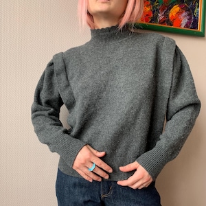 May include: A gray turtleneck sweater with a slightly puffed shoulder design.