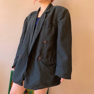 Könnte beinhalten: Dunkelgrüner Blazer mit doppelreihigem Design. Der Blazer hat zwei Reihen brauner Knöpfe und zwei Vordertaschen. Der Stoff scheint leicht zu sein, geeignet für das Tragen in Schichten. Der Blazer ist im Vintage-Stil.