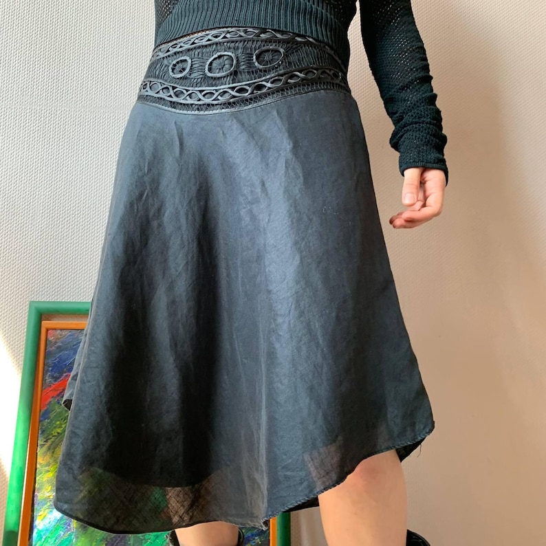 K&ouml;nnte beinhalten: Ein schwarzer Rock mit dekorativem Bund. Der Rock hat eine ausgestellte Silhouette und besteht aus einem leichten, transparenten Stoff. Der Bund weist ein aufwendiges Design mit kreisf&ouml;rmigen und geometrischen Mustern auf. Teil einer Bekleidungskollektion.