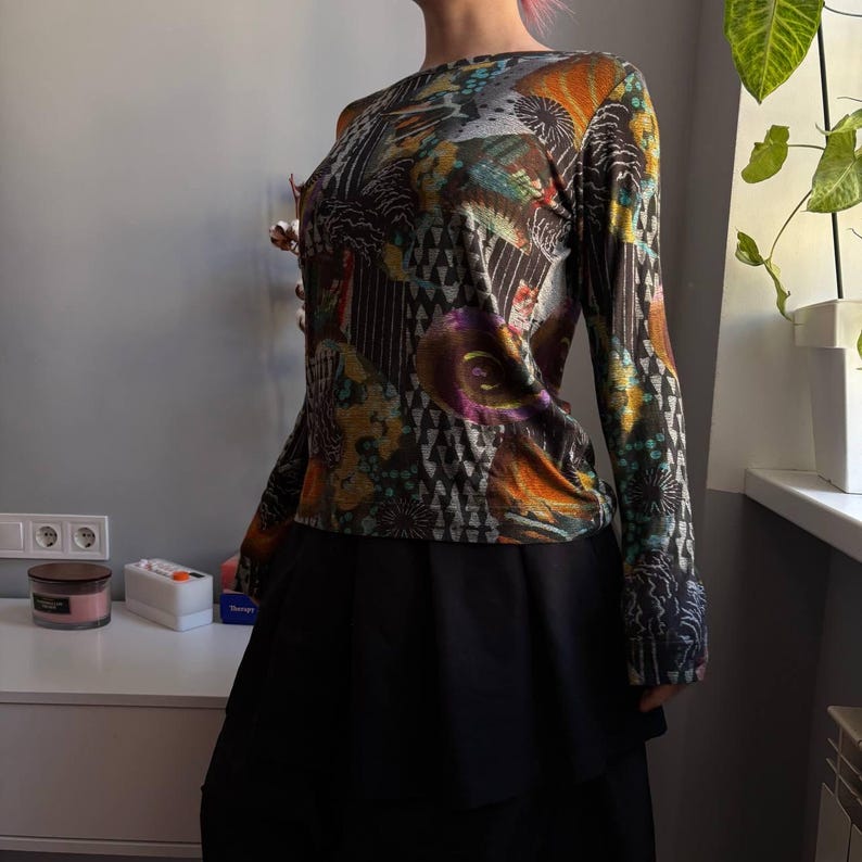 Puede incluir: Una blusa de manga larga con un estampado abstracto colorido en tonos marr&oacute;n, naranja, turquesa y morado. La blusa se combina con una falda negra. El dise&ntilde;o presenta formas geom&eacute;tricas y florales.