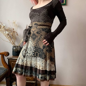 Può includere: Abito marrone a maniche lunghe con motivo. L'abito presenta uno scollo tondo, un corpetto aderente e una gonna ampia con un bordo decorativo. Una cintura abbinata stringe la vita. L'abito è in stile bohémien.