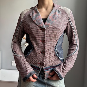 May include: A patchwork blazer in shades of red, blue, and grey. The jacket features a woven pattern with denim accents and floral patterned lapels. It has three brown buttons and a tailored fit.